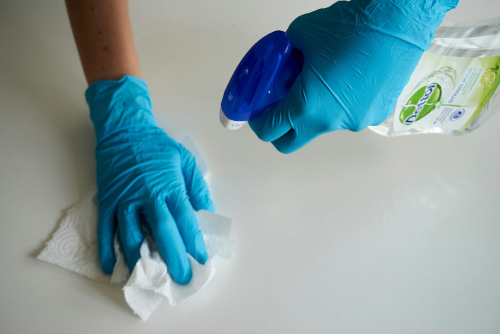 Nahaufnahme einer Person in blauen Latex-Handschuhen, die am putzen ist. Man sieht nur die Hände